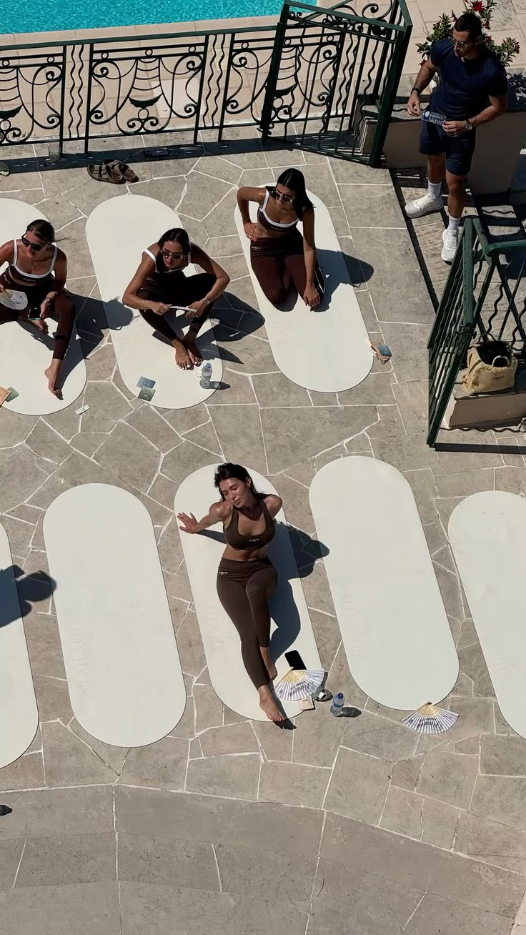 Guests practicing Pilates on mats beside a pool in the sun